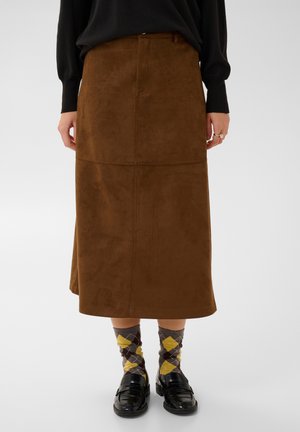 Mannequin portant une jupe midi marron façon daim, un haut noir, des chaussettes à losanges jaunes et grises et des mocassins noirs.