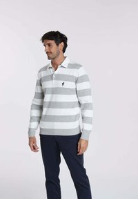 Pull à rayures en tissu tricoté gris et blanc, avec un col polo, des manches longues, des poignets côtelés et un petit logo sur la poitrine gauche.