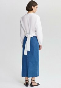 Weißes Langarmbluse mit Bindeband und hohem Kragen, kombiniert mit einem langen blauen Jeansrock und schwarzen flachen Schuhen mit Riemen.