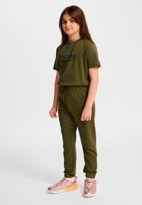 Conjunto a juego de camiseta y pantalones deportivos en verde oliva con cintura de cordón; combinado con zapatillas brillantes en oro rosa. Diseño casual y cómodo.