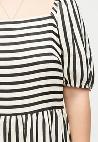 Κοντινή λήψη ενός ασπρόμαυρου ριγέ φορέματος με φουσκωτά κοντά μανίκια και τετράγωνη λαιμόκοψη στο πάνω μέρος του κορμού ενός ατόμου.