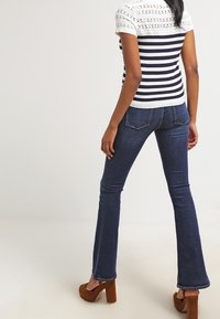 Top de manga corta a rayas azul marino y blancas con detalle de encaje; combinado con vaqueros acampanados azul oscuro y zapatos marrones de tacón.