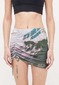 Falda corta con frunces en tejido suave, que presenta un patrón degradado de verde y gris, con un diseño impreso que incluye texto y acentos florales.