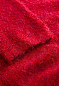 Rød tekstureret stof med en blød, fuzzy udseende, der har en blanding af fibre og subtile variationer i nuancer over hele overfladen.