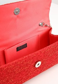 Czerwona koronkowa portmonetka z gładką satynową podszewką, z metalowym zatrzaskiem, klipsem na brelok oraz wewnętrznymi kieszonkami na karty. Widoczna metka wewnątrz.