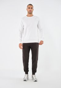 Sudadera blanca de cuello redondo con mangas raglán, combinada con joggers negros y zapatillas deportivas grises. Textura suave, diseño casual.
