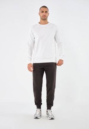 Witte sweatshirt met ronde hals en raglanmouwen, gecombineerd met zwarte joggers en grijze sportschoenen. Zachte textuur, casual ontwerp.