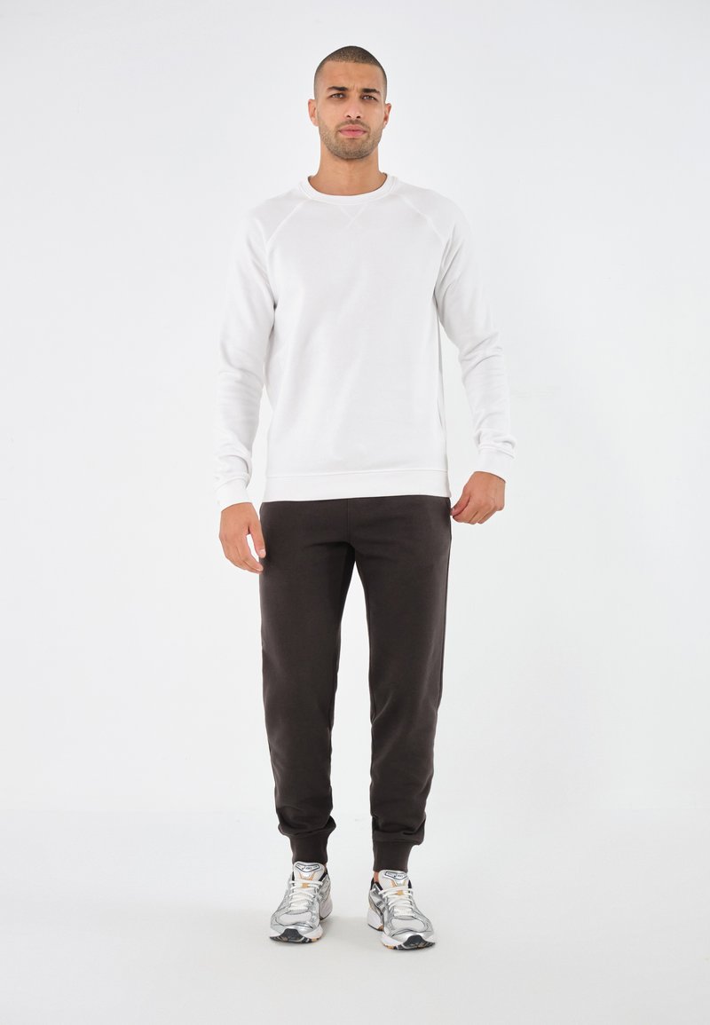 Sudadera blanca de cuello redondo con mangas raglán, combinada con joggers negros y zapatillas deportivas grises. Textura suave, diseño casual.