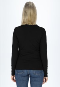 Maglietta nera a maniche lunghe con design aderente. Tessuto morbido, scollatura rotonda e maniche slim, abbinata a jeans blu.
