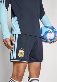 Camisa de futebol azul escura com detalhes em azul claro e logótipo da AFA, acompanhada de calções combinando com bordados dourados e três riscas.