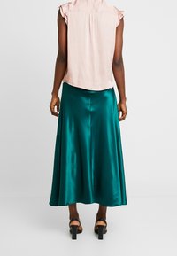 Maxikjol i satin i färgen tealfärgad med ett flödande mönster, kombinerad med en ljusrosa blus med korta ärmar; kännetecknas av en mjuk textur och subtil glans.