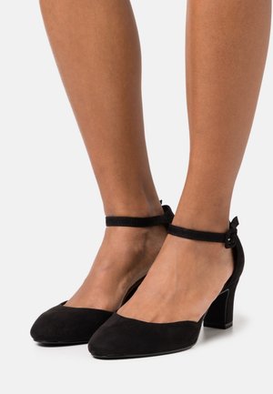 Talons noirs en daim avec une sangle de cheville, un bout carré et un talon bloc bas. La sangle est dotée d'une boucle pour un ajustement sécurisé.