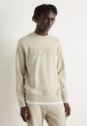 Felpa color beige chiaro con logo "BOSS" in una tonalità coordinata. Presenta un colletto rotondo, polsini a costine e una texture liscia. Abbinata a pantaloni beige.