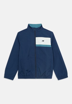 Veste légère bleu marine avec fermeture éclair frontale, col montant, poignets et ourlet élastiques, panneau poitrine blanc et turquoise avec petit logo.