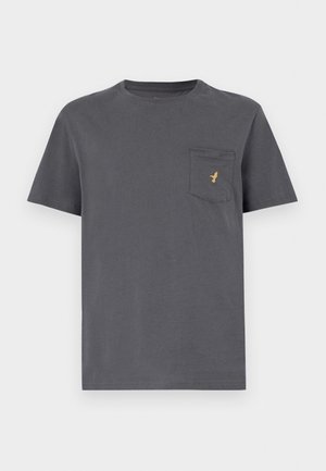 Szürke pamut póló rövid ujjakkal, kerek nyakkal, és egy zsebbel, amelyen bal oldalán egy kis arany logó található. Simább anyagtextúra.