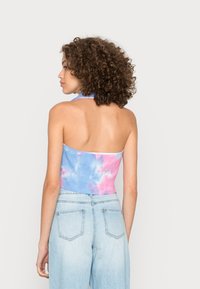 Top cropped em tie-dye nas cores azul e rosa, textura canelada, design de alças, combinado com jeans claros de cintura alta.