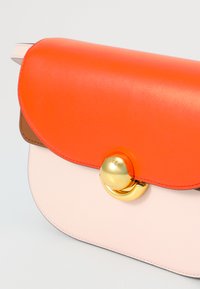 Bolso de mano multicolor con una tapa de cuero naranja suave, un cuerpo rosa pálido y hardware circular dorado con logotipo en relieve.