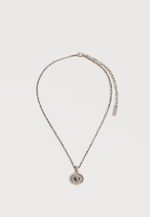 Collier chaîne en argent avec pendentif rond présentant une tête de lion détaillée entourée de petites pierres claires, fermoir mousqueton et chaîne d'extension.