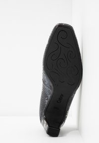 Černá texturovaná bota s hadím vzorem, nízkým podpatkem a gumovou podrážkou s detailním designem. Logo značky je viditelné na podrážce.