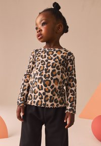 Leopard print long-sleeve top with ribbed texture, beige base, and black-brown spots; features scalloped hem. Paired with black loose-fitting pants.