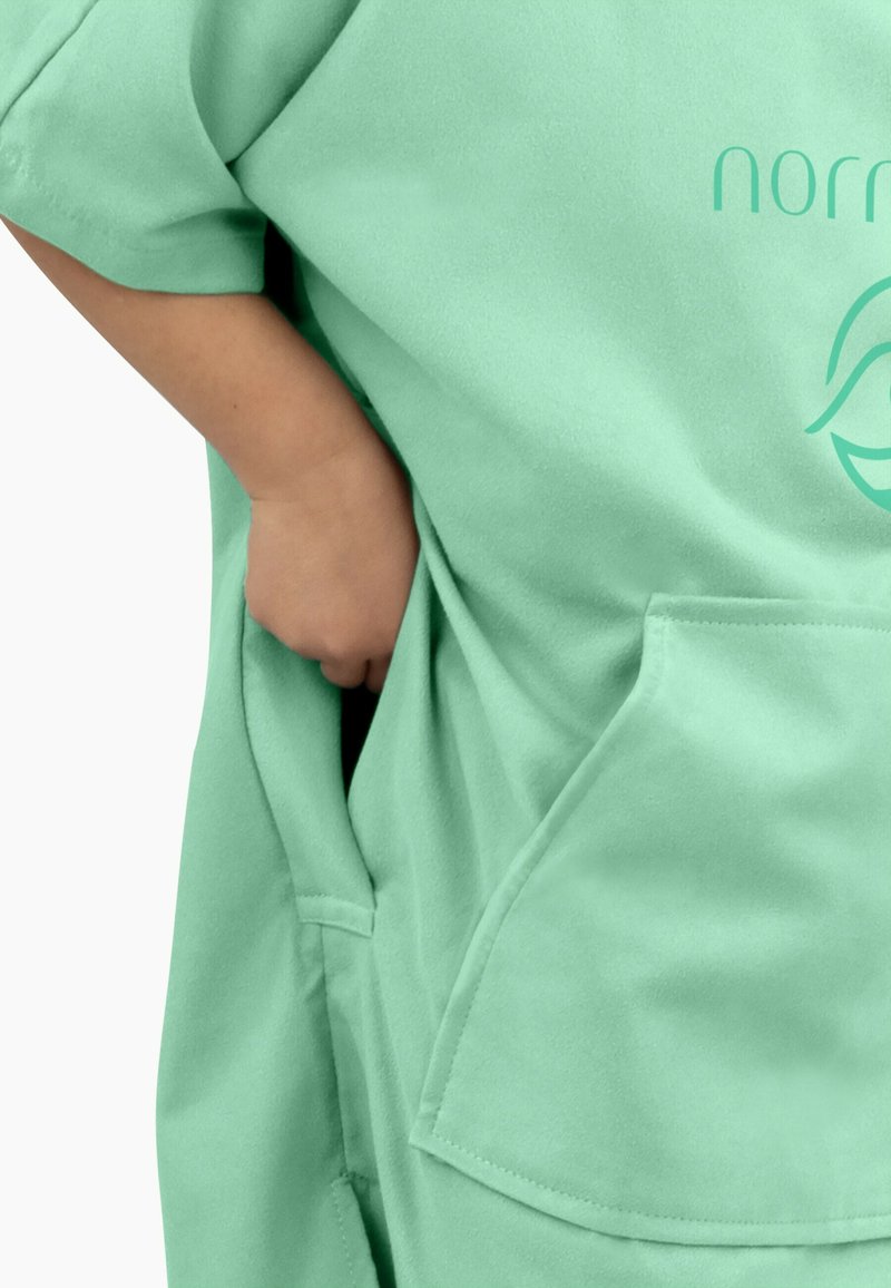 Mintgrünes, oversized Kleidungsstück mit kurzen Ärmeln, ausgestattet mit einer Vordertasche und einer glatten Textur. Logo in einem helleren Grün aufgedruckt.