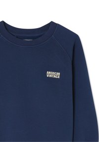 Laivastonsininen collegepaita, jossa on resorinen pyöreä pääntie, raglanhihat ja pieni valkoinen "AMERICAN VINTAGE" -logo rinnassa. Pehmeä tekstuuri.