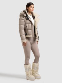 Giacca imbottita beige con fodera in pelliccia sintetica, abbinata a leggings beige chiaro e stivali da neve bianchi con lacci e dettagli testurizzati.