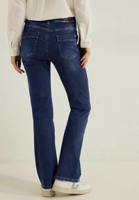 Vaqueros bootcut de color azul oscuro, hechos de denim, con una cintura de altura media, dos bolsillos traseros y una sutil textura deslavada en el dobladillo.