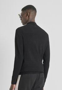 Zwarte gebreide trui met een geribbelde kraag en een textuur op het achterpand, met aansluitende mouwen en een rechte snit ter hoogte van de taille.