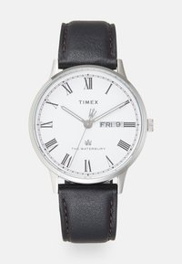 Reloj Timex Waterbury con esfera blanca, números romanos, manecillas plateadas y correa de piel negra con costuras en contraste.