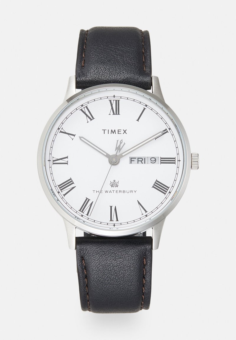 Zegarek Timex Waterbury z białą tarczą, rzymskimi cyframi, srebrnymi wskazówkami oraz czarnym skórzanym paskiem z kontrastowym przeszyciem.