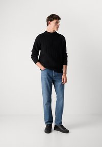 Black ribbed knit sweater with a high neck, paired with light blue straight-leg jeans and black lace-up sneakers. Minimalist design.