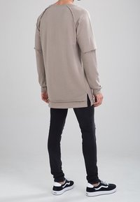 Camisa de manga larga beige claro con diseño de manga raglán y bordes deshilachados, combinada con unos pantalones negros ajustados y calzado negro.