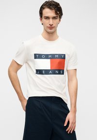Λευκό κοντομάνικο μπλουζάκι με ορθογώνιο σχέδιο σε ναυτικό μπλε, λευκό και κόκκινο, με το κείμενο "TOMMY JEANS". Ομαλή βαμβακερή υφή.