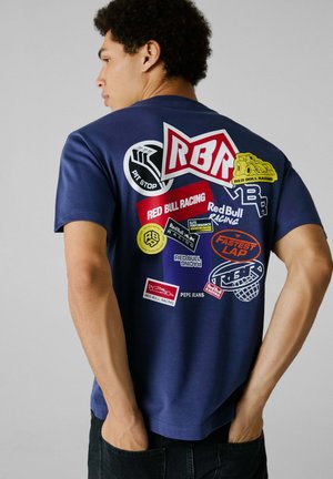 Navy blue T-shirt featuring multiple colorful patches, including logos from Red Bull Racing, with short sleeves and a relaxed fit.
