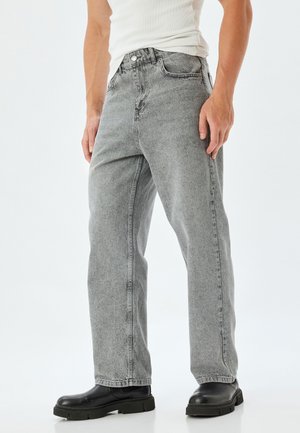 Jeans de denim gris con un corte relajado, cinco bolsillos y una cintura alta. Presenta un ligero desgaste y un diseño de pierna recta, combinados con botas negras.