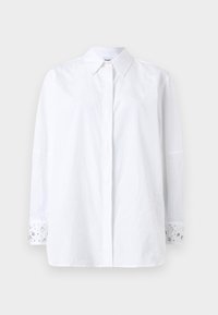 Λευκό πουκάμισο με κουμπιά, μακριά μανίκια και γιακά. Οι μανσέτες διακοσμούνται με κοσμήματα και λουλουδάτο σχέδιο. Κατασκευασμένο από αδιαφανές ύφασμα.