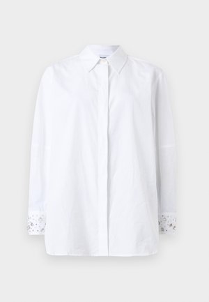 Hvit skjorte med knapper, lange ermer og krage. Mansjettene har dekorative juveler og et blomsterdesign. Laget av ugjennomsiktig stoff.