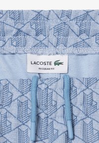 Lichtblauwe stof met geometrische patronen, voorzien van een Lacoste-label met de tekst "Regular Fit" en twee bijpassende trekkoorden.