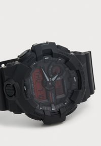 Montre-bracelet analogique-numérique en plastique noir avec un design épais, un affichage numérique rouge, plusieurs boutons et des accents texturés. Étanche jusqu'à 200 mètres.