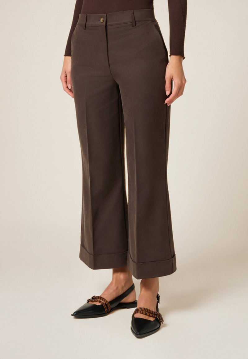 Pantalones de pierna ancha marrón oscuro con una textura suave, que presentan un cierre frontal con botón y dobladillos enrollados. Combinados con unas bailarinas negras de punta afilada.