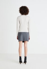 Hellbeige, gerippter Langarm-Top, kombiniert mit einem grauen Minirock. Das Model trägt schwarze Knöchelstiefel mit spitzen Absätzen. Glatte Texturen sind sichtbar.