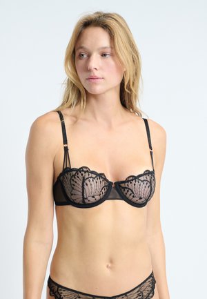 Soutien-gorge en dentelle noire avec un matériau transparent, des bords festonnés, un motif à pois et des bretelles réglables. Armatures pour le soutien. Détails de conception délicats.