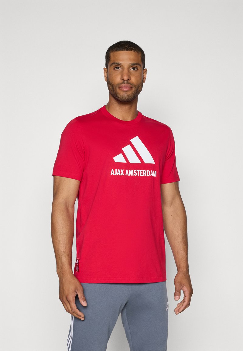 Rød bomulds T-shirt med hvid "AJAX AMSTERDAM" logo og tre stribede accenter. Kortærmet med rund hals.