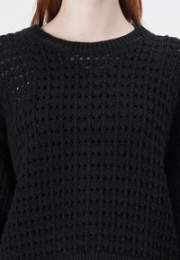 Pull noir en tricot avec un motif ajouré texturé, encolure ronde et poignets côtelés. Le tissu semble doux et respirant.