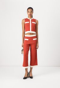 Twee-delig outfit met een mouwloze rode crop top met een gestructureerd patroon en bijpassende wijde broek, afgewerkt met witte accenten.