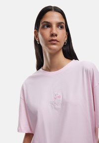 Lyserød bomulds T-shirt med korte ærmer og rund halsudskæring, prydet med et broderet hvidt katte-design med en lyserød sløjfe.