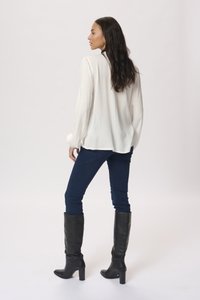 White long-sleeve blouse, blue skinny jeans, and knee-high black leather heeled boots. The blouse is lightweight with a loose fit.