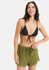 Čierny trojuholníkový bikiny top s viazaním vpredu, skombinovaný s olivovozelenými háčkovanými šortkami s viazaním v páse a textúrovaným vzorom.
