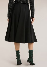 Sort, knælange skørt med vidde lavet af et tekstureret stof, med en glat taljebånd. Kombineret med grønne, ribbede sokker og høje sandal med hæl.